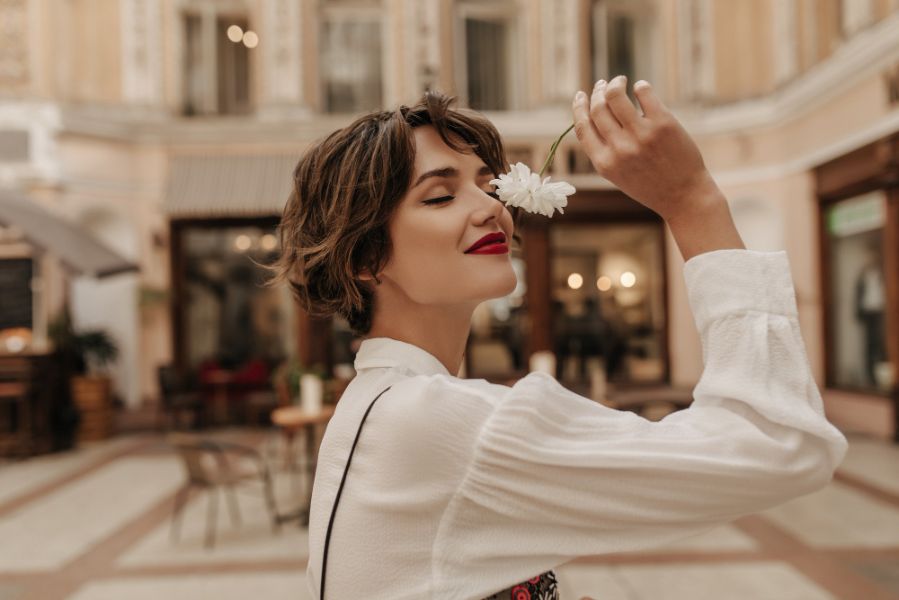 Femme sentant une fleur en extérieur illustrant la perception personnelle des notes parfumées selon la peau et la sensibilité olfactive