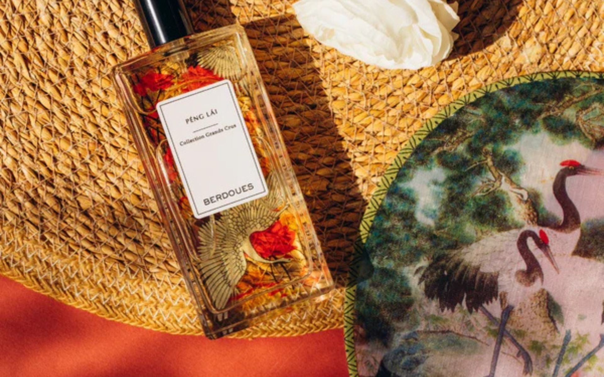 Flacon de parfum Berdoues posé sur une surface tressée, entouré d’éléments décoratifs, illustrant la diffusion et la persistance du sillage olfactif
